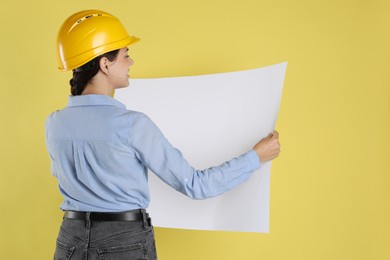 Engineer in hard hat with draft on yellow background, space for text