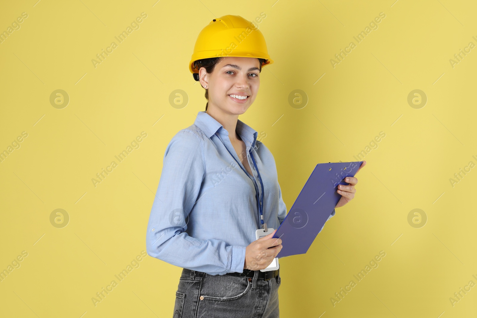 Photo of Engineer in hard hat with clipboard on yellow background