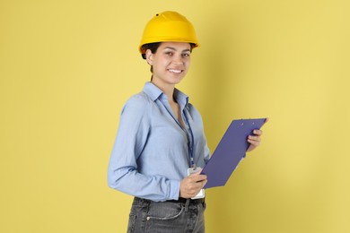 Engineer in hard hat with clipboard on yellow background