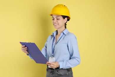 Engineer in hard hat with clipboard on yellow background