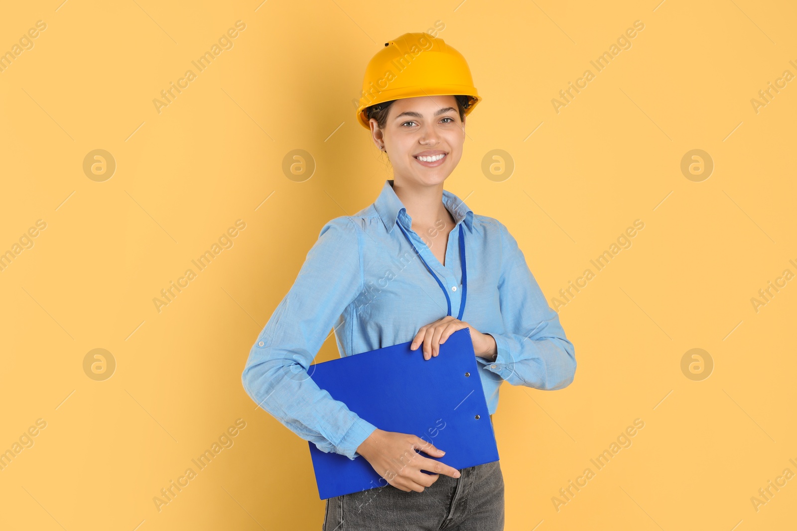 Photo of Engineer in hard hat with clipboard on yellow background