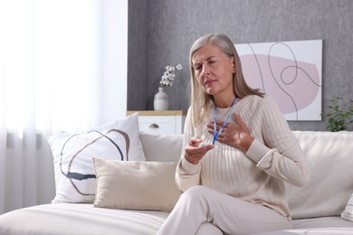 Photo of Senior woman suffering from heart pain holding emergency call button at home