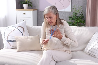 Senior woman suffering from heart pain holding emergency call button at home