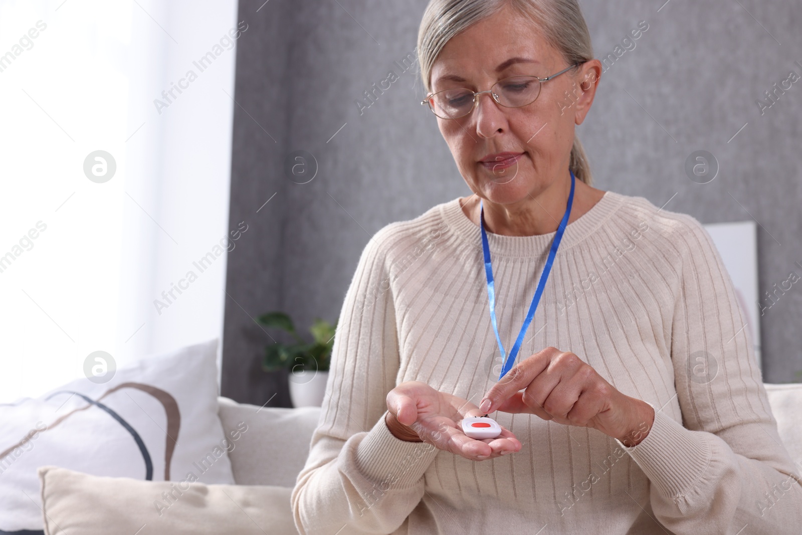 Photo of Senior woman in glasses pressing emergency call button at home