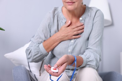 Photo of Senior woman suffering from heart pain pressing emergency call button at home, closeup