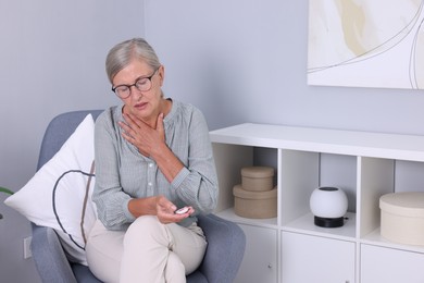 Photo of Senior woman suffering from neck pain holding emergency call button at home