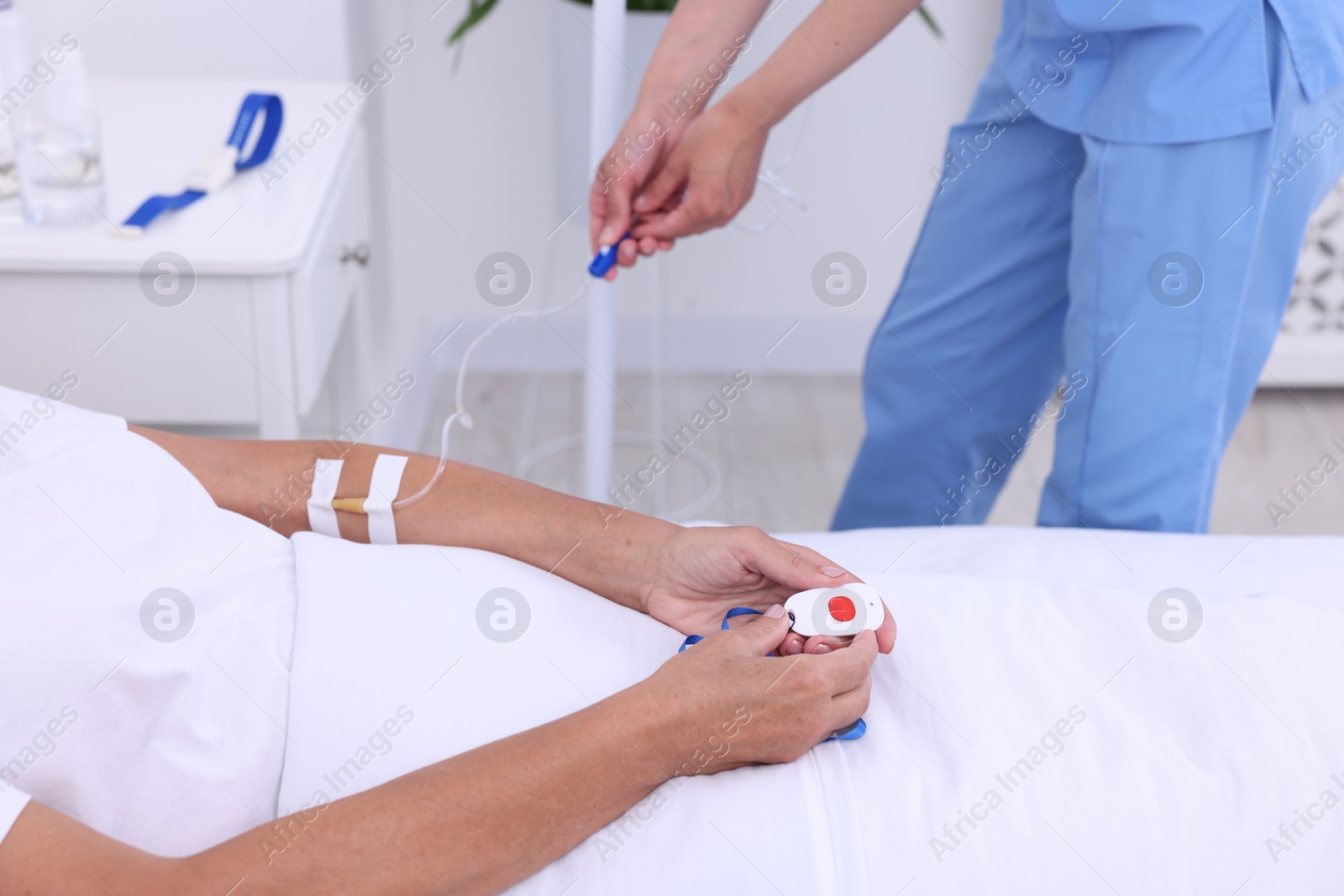 Photo of Senior woman with emergency call button and nurse setting IV drip in hospital, closeup