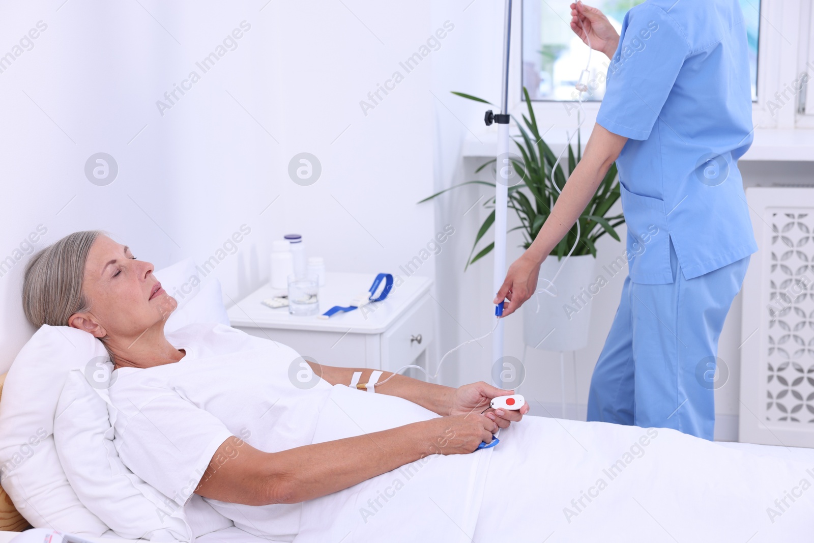 Photo of Senior woman with emergency call button and nurse setting IV drip in hospital