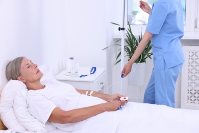 Senior woman with emergency call button and nurse setting IV drip in hospital