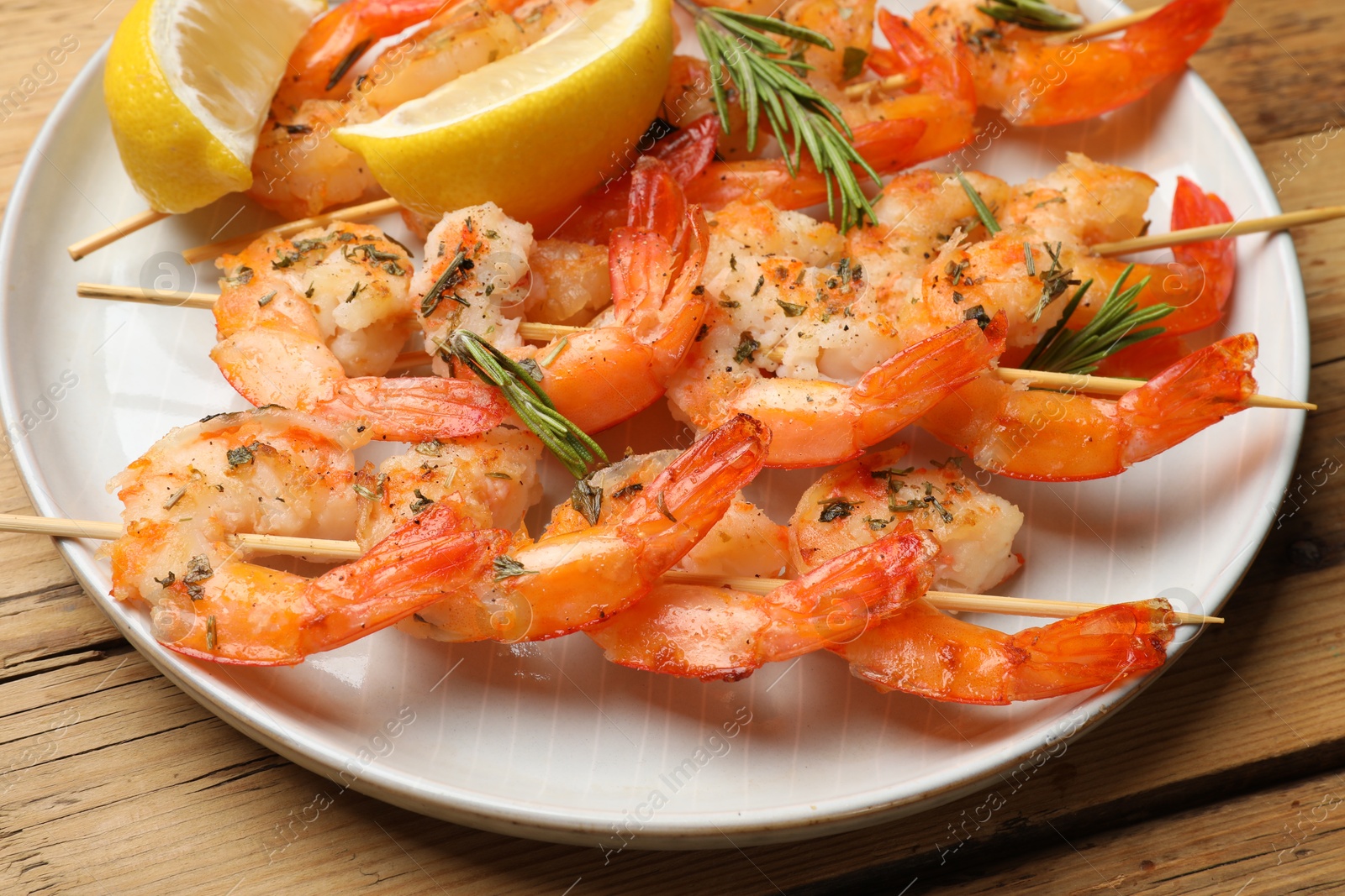 Photo of Skewers with delicious grilled shrimps served on wooden table, closeup