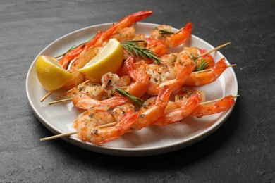 Photo of Skewers with delicious grilled shrimps served on black table, closeup