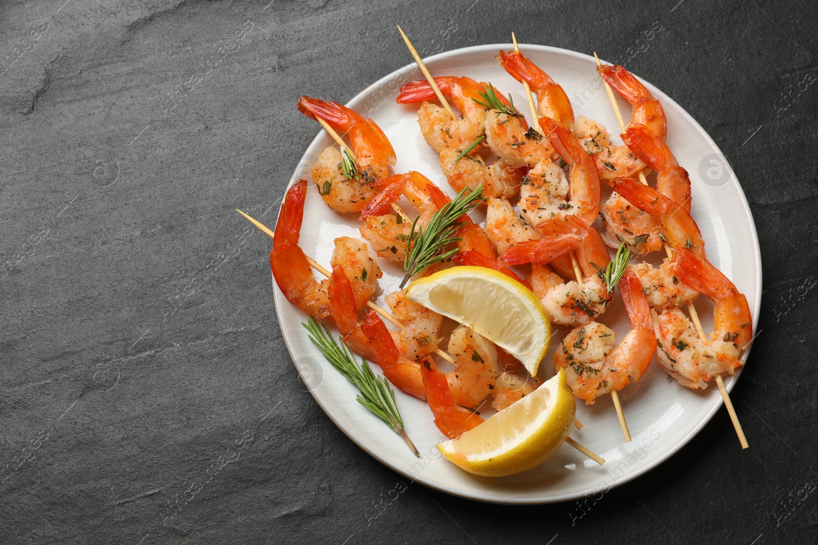 Photo of Skewers with delicious grilled shrimps served on black table, top view. Space for text