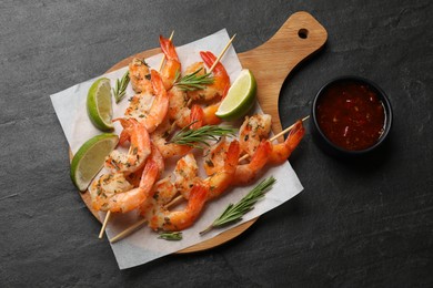 Photo of Delicious grilled shrimp skewers served with sauce and lime on black table, top view