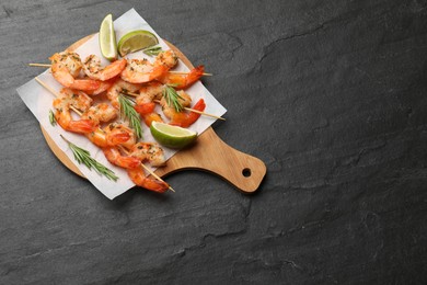 Photo of Skewers with delicious grilled shrimps served on black table, top view. Space for text