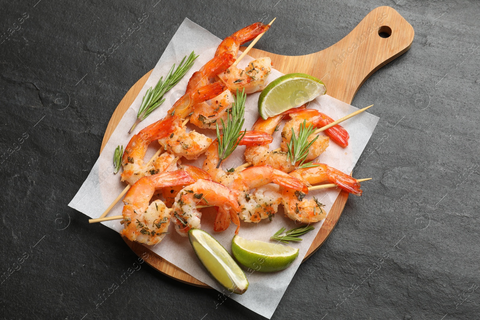 Photo of Skewers with delicious grilled shrimps served on black table, top view