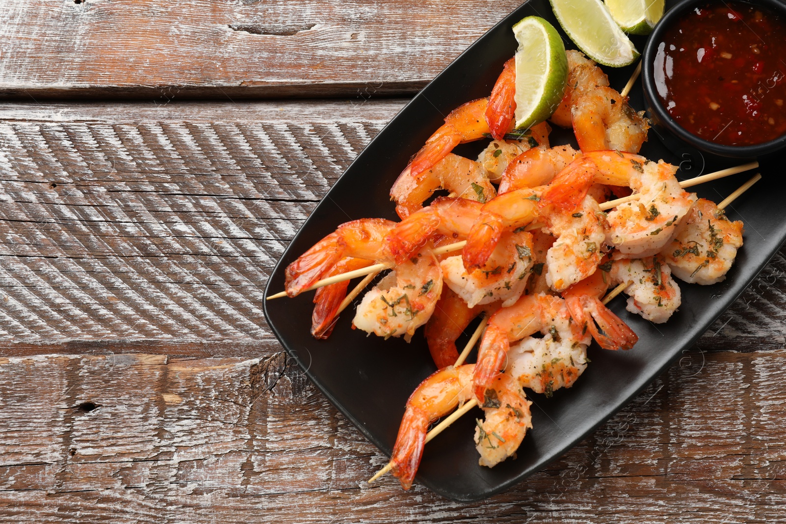 Photo of Delicious grilled shrimp skewers served with sauce and lime on wooden table, top view. Space for text