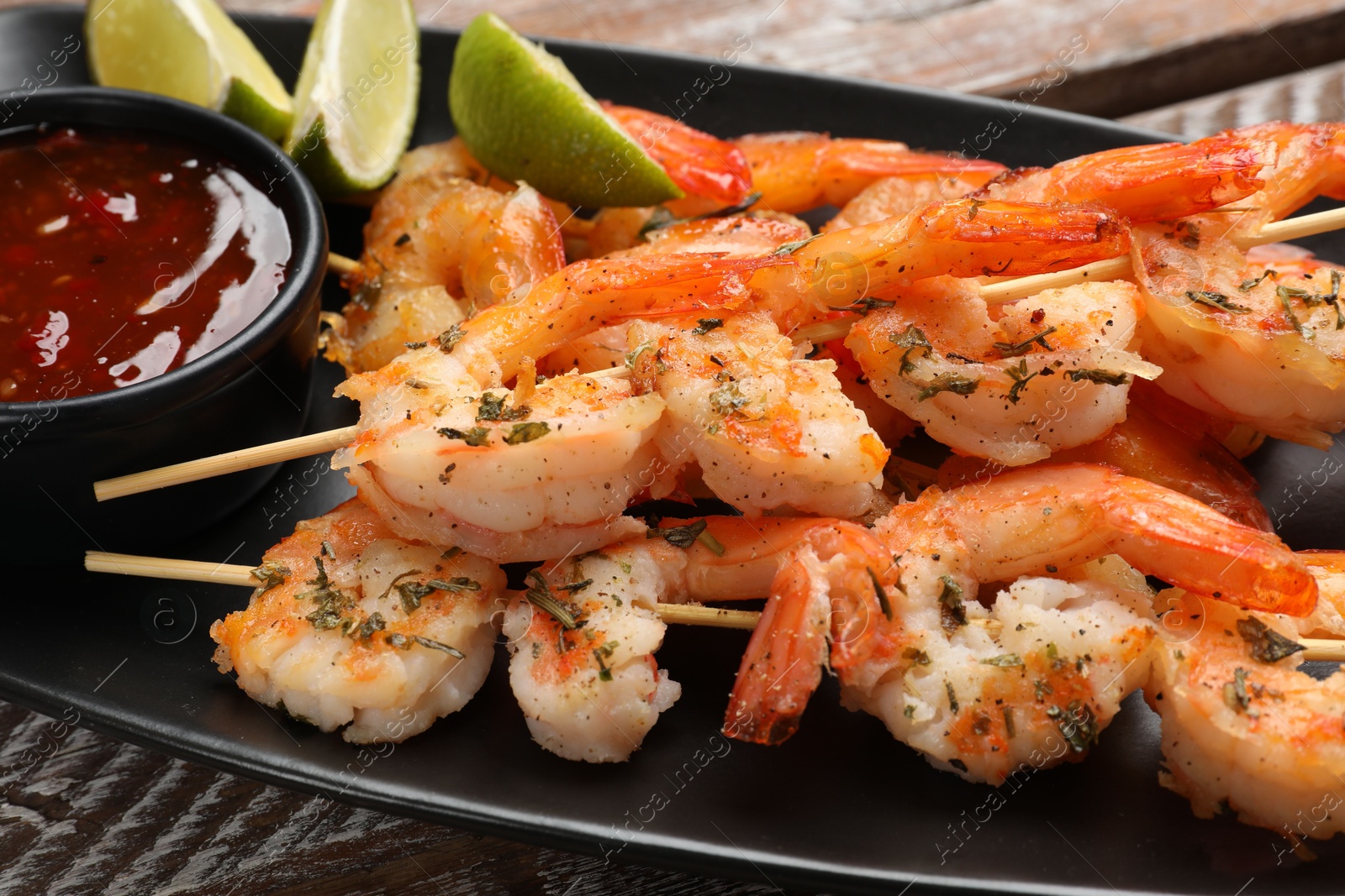 Photo of Delicious grilled shrimp skewers served with sauce and lime on wooden table, closeup