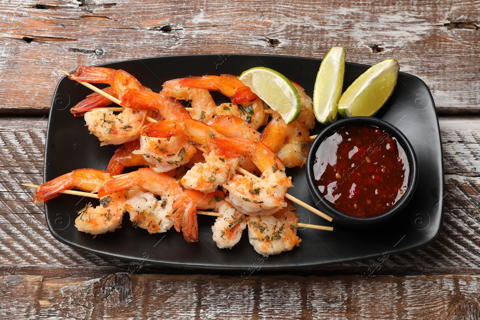 Photo of Delicious grilled shrimp skewers served with sauce and lime on wooden table, top view