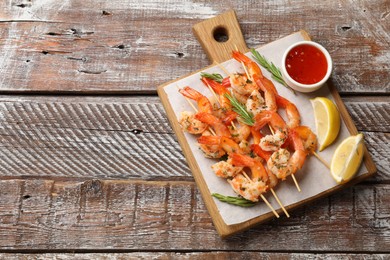 Photo of Delicious grilled shrimp skewers served with sauce and lemon on wooden table, top view. Space for text