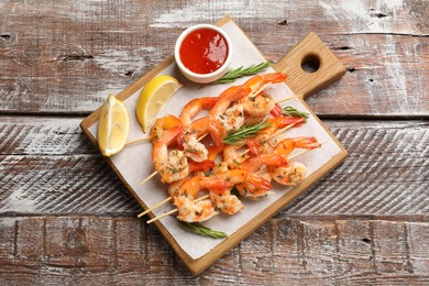 Photo of Delicious grilled shrimp skewers served with sauce and lemon on wooden table, top view