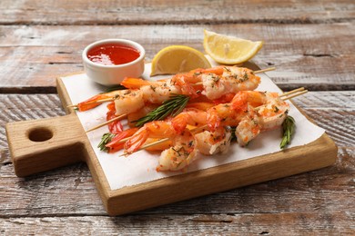 Photo of Delicious grilled shrimp skewers served with sauce and lemon on wooden table