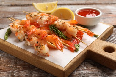 Photo of Delicious grilled shrimp skewers served with sauce and lemon on wooden table, closeup