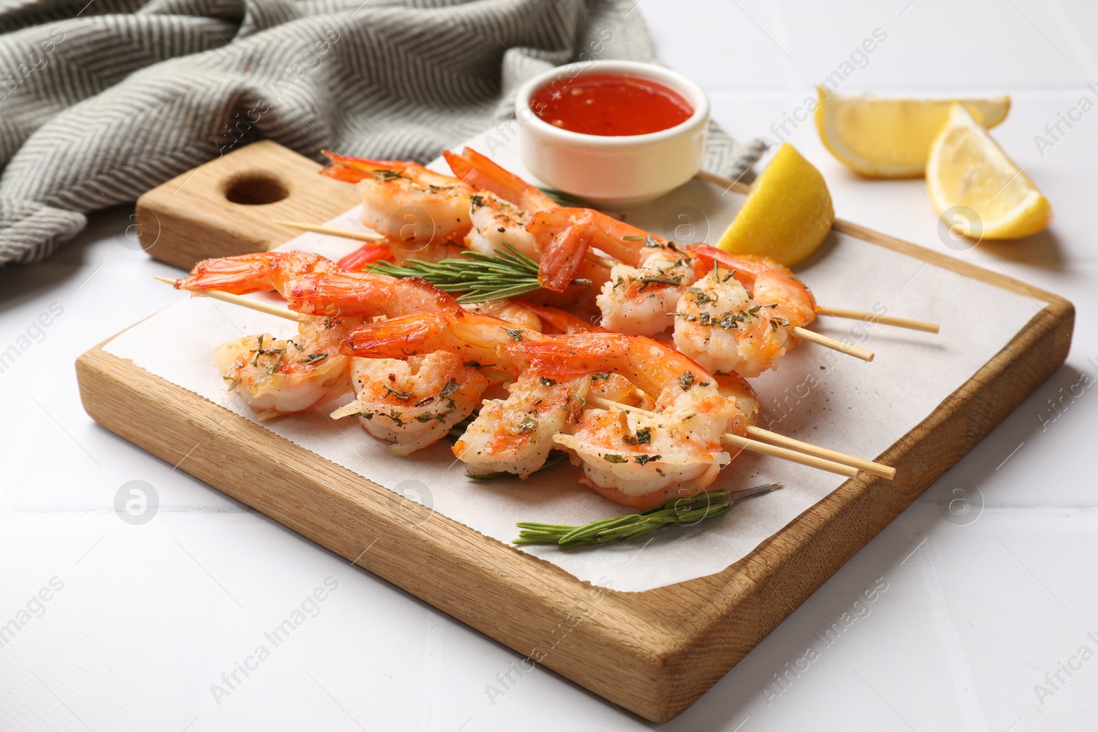 Photo of Delicious grilled shrimp skewers served with sauce and lemon on white tiled table