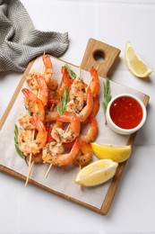 Photo of Delicious grilled shrimp skewers served with sauce and lemon on white table, top view