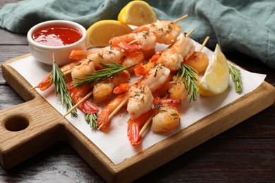 Photo of Delicious grilled shrimp skewers served with sauce and lemon on wooden table, closeup