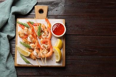 Photo of Delicious grilled shrimp skewers served with sauce and lemon on wooden table, top view. Space for text