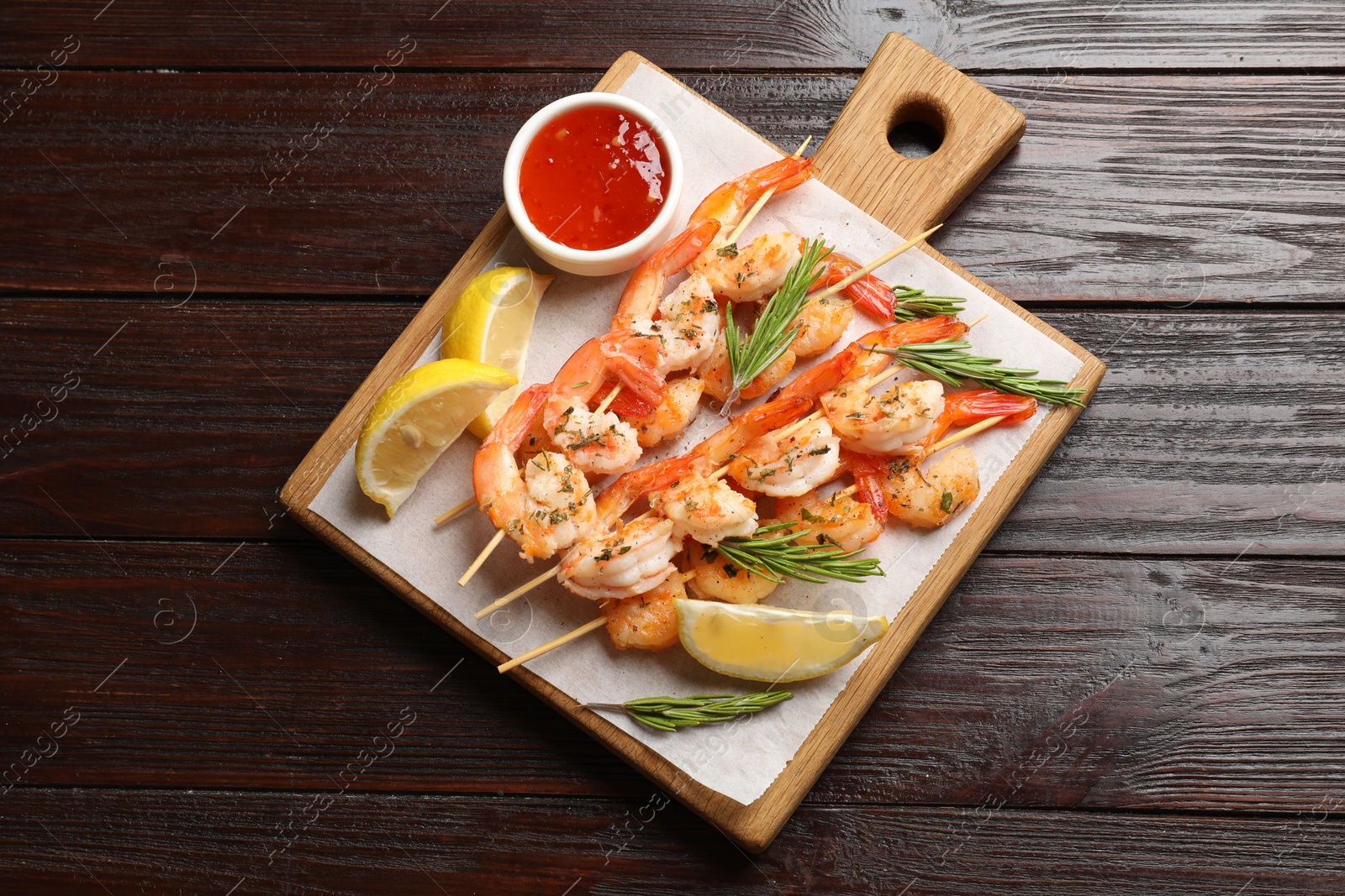 Photo of Delicious grilled shrimp skewers served with sauce and lemon on wooden table, top view