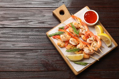 Photo of Delicious grilled shrimp skewers served with sauce and lemon on wooden table, top view. Space for text