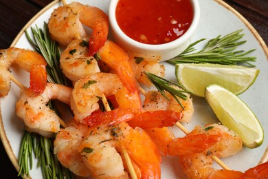 Photo of Delicious grilled shrimp skewers served with sauce and lime on wooden table, closeup