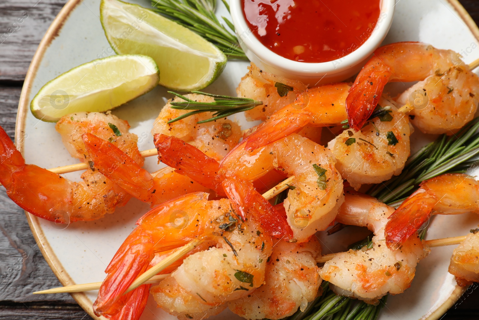 Photo of Delicious grilled shrimp skewers served with sauce and lime on wooden table, top view