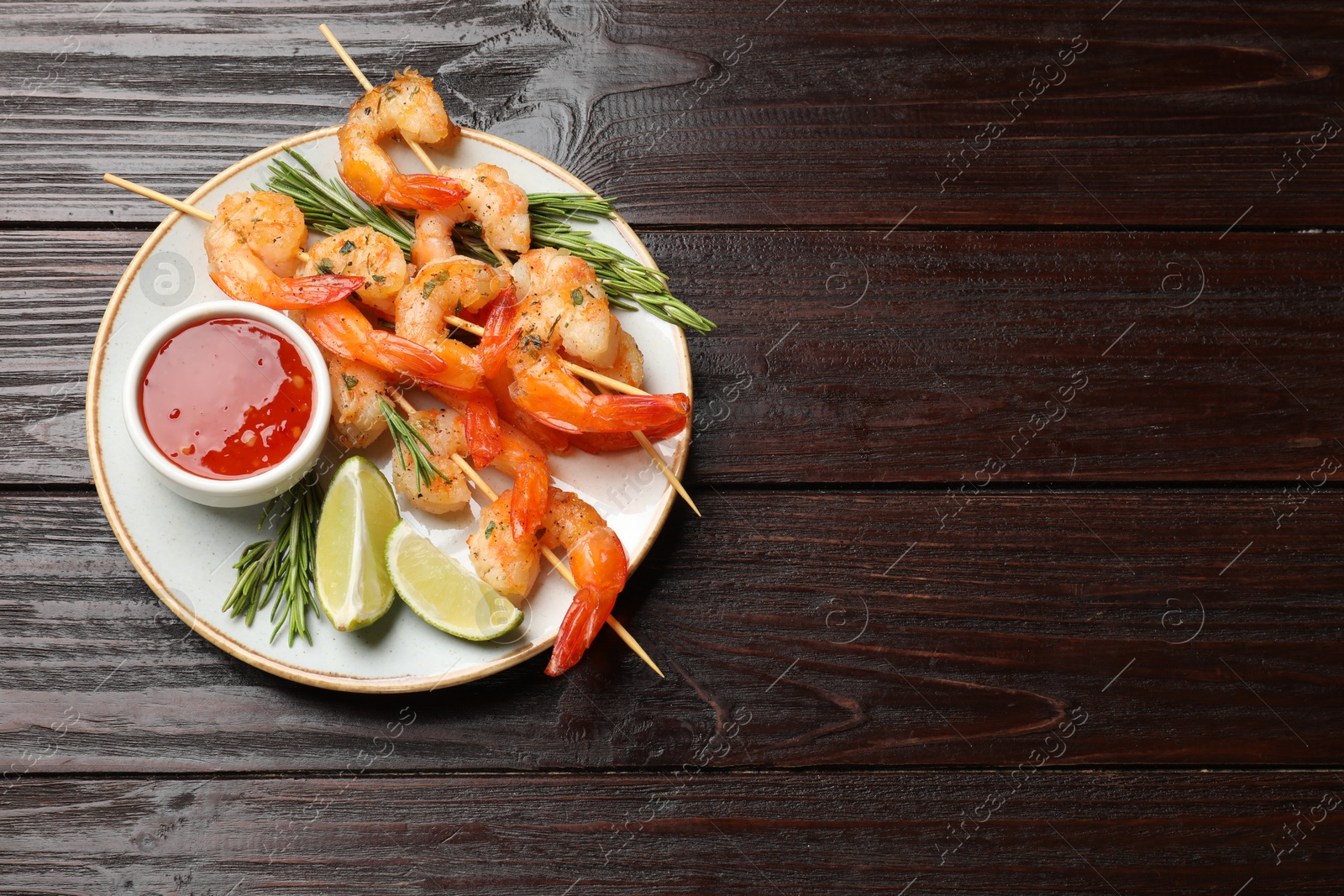 Photo of Delicious grilled shrimp skewers served with sauce and lime on wooden table, top view. Space for text