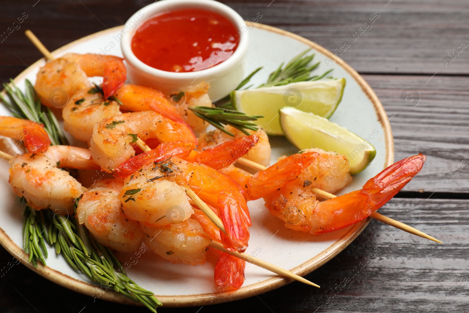 Photo of Delicious grilled shrimp skewers served with sauce and lime on wooden table, closeup