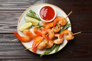 Photo of Delicious grilled shrimp skewers served with sauce and lime on wooden table, top view