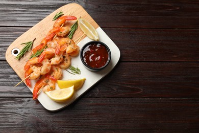 Photo of Delicious grilled shrimp skewers served with sauce and lemon on wooden table, top view. Space for text