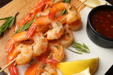 Photo of Delicious fresh shrimp skewers served with sauce and lemon on board, closeup