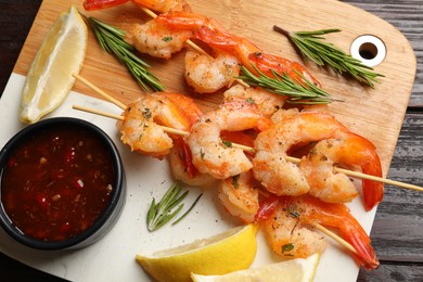 Photo of Delicious grilled shrimp skewers served with sauce and lemon on wooden table, top view