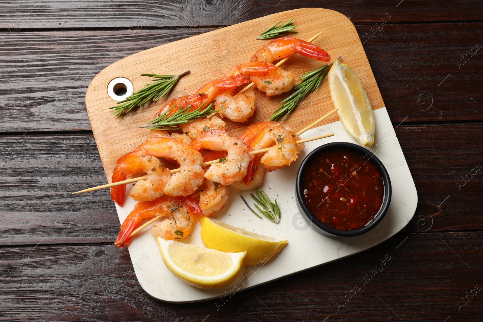 Photo of Delicious grilled shrimp skewers served with sauce and lemon on wooden table, top view