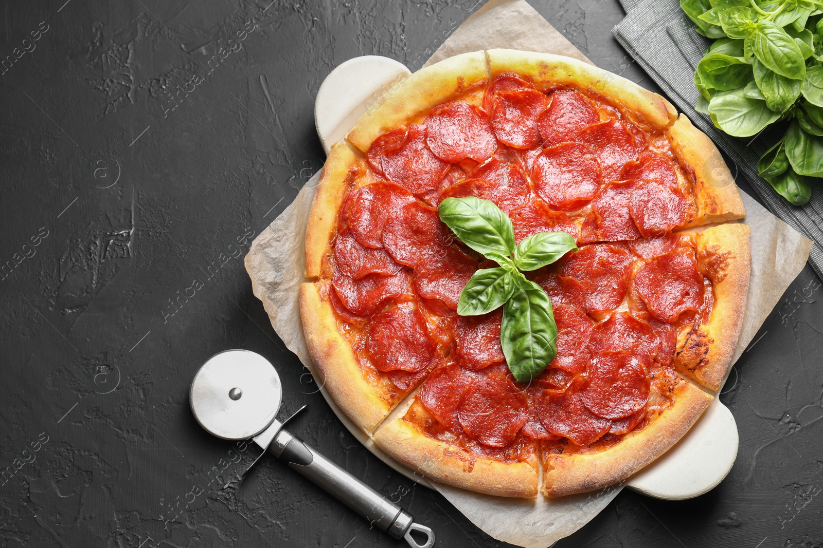 Photo of Tasty pepperoni pizza, cutter and basil on black textured table, flat lay. Space for text