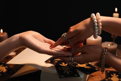 Fortune teller reading lines on woman's palm at wooden table, closeup. Chiromancy