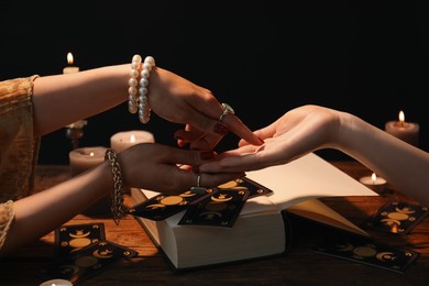 Fortune teller reading lines on woman's palm at wooden table, closeup. Chiromancy