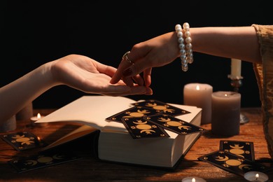 Photo of Fortune teller reading lines on woman's palm at wooden table, closeup. Chiromancy