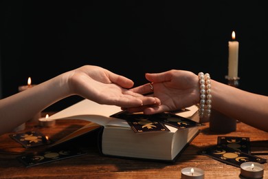 Fortune teller reading lines on woman's palm at wooden table, closeup. Chiromancy