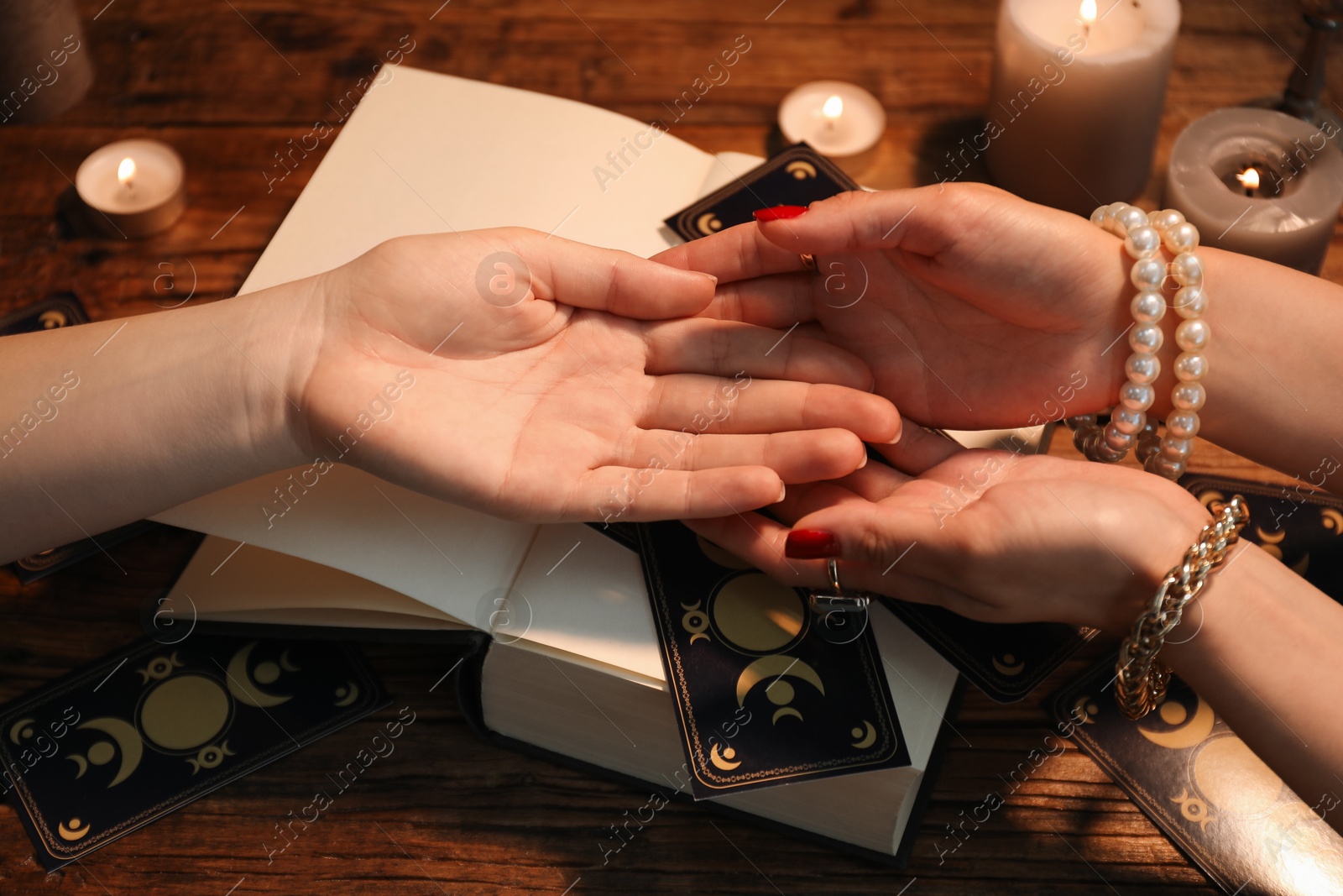 Photo of Fortune teller reading lines on woman's palm at wooden table, closeup. Chiromancy