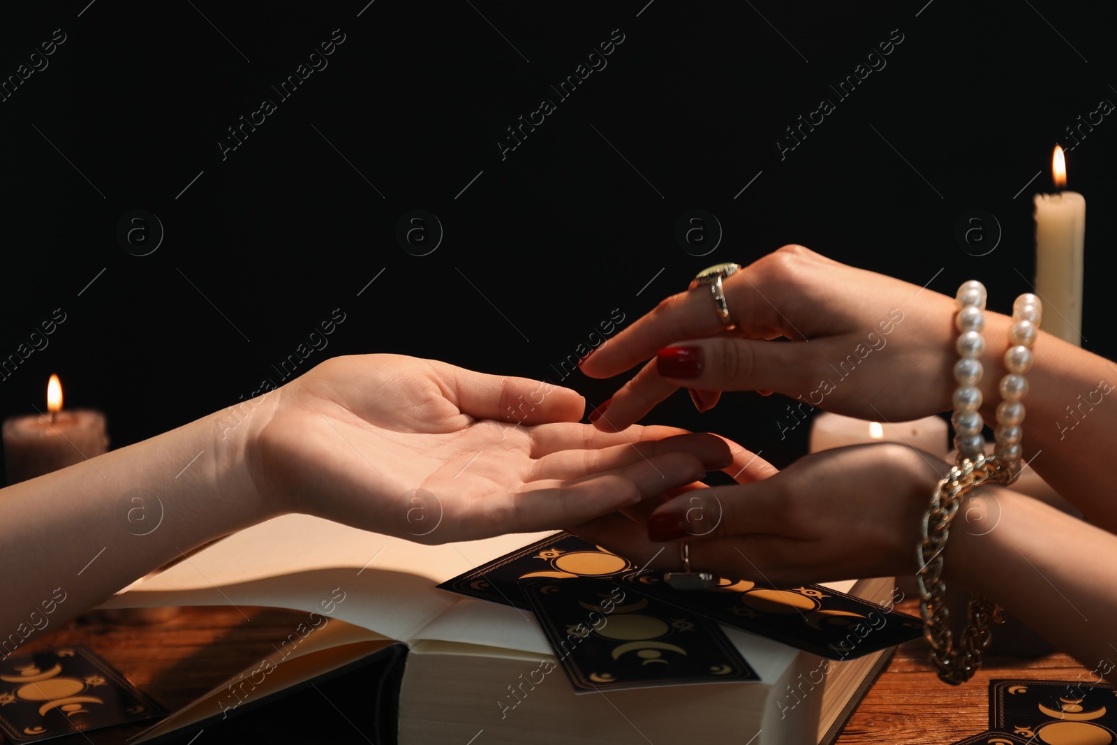 Photo of Fortune teller reading lines on woman's palm at wooden table, closeup. Chiromancy