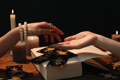 Photo of Fortune teller reading lines on woman's palm at wooden table, closeup. Chiromancy