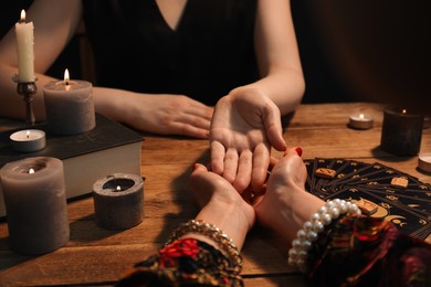 Fortune teller reading lines on woman's palm at wooden table, closeup. Chiromancy